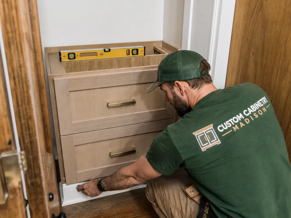 Installer fitting and leveling a base cabinet and drawer stack inside a reach-in closet with careful scribing to trim